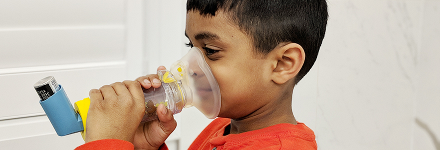 Young boy uses an inhaler and an aerochamber to take a medication to treat asthma