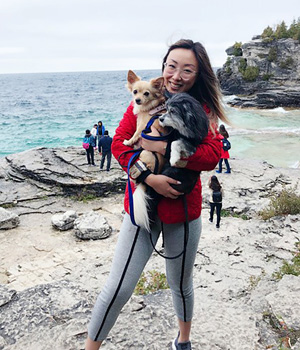 Jenny Liu holding her two dogs by a rocky beach