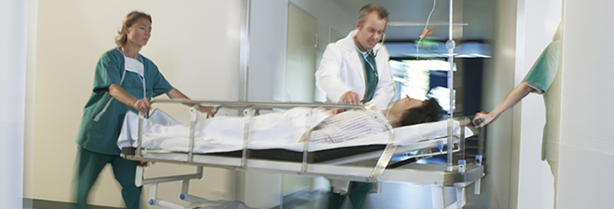 Patient being moved on a rolling bed by a nurse and a physician listening to the patients chest. 