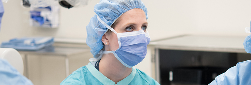 A female physician in an operating room wearing a green mask.