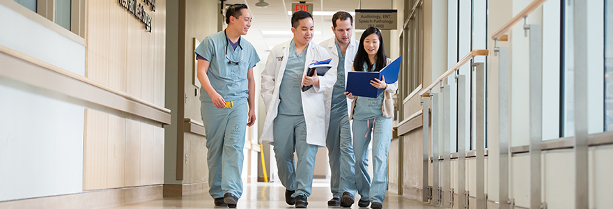 Three male and one female resident walking down a hospital hallway holding blue binders. 