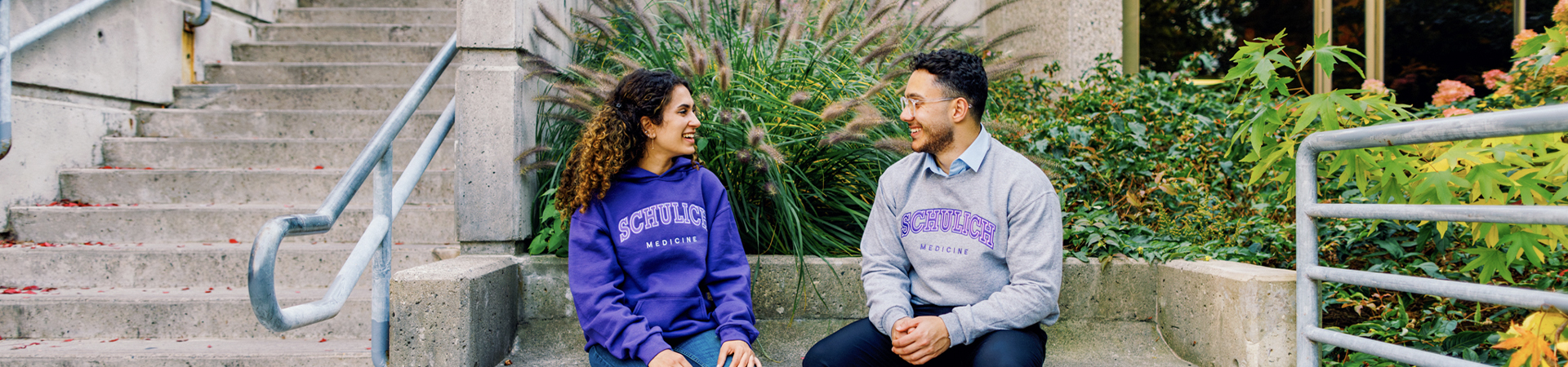 Two students sitting and talking outdoors near a building