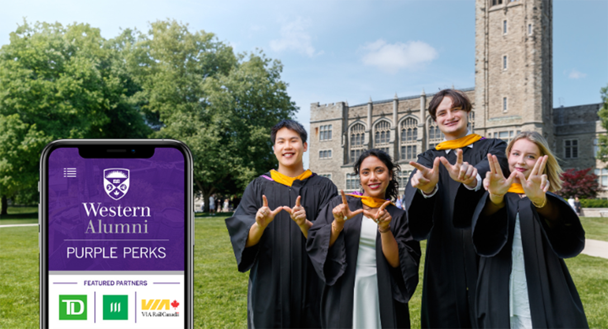 Recent graduates standing on campus beside a Western Alumni Purple Perks mobile app display.