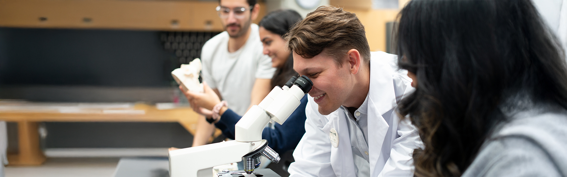 Students in a lab, one using a microscope.