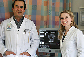 White female wearing a white coat standing infront of an ultrasound machine