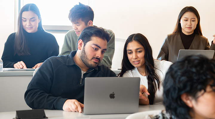 Group of five Schulich Medicine students laughing and talking together indoors, with two standing arm in arm and three seated, enjoying a casual conversation.