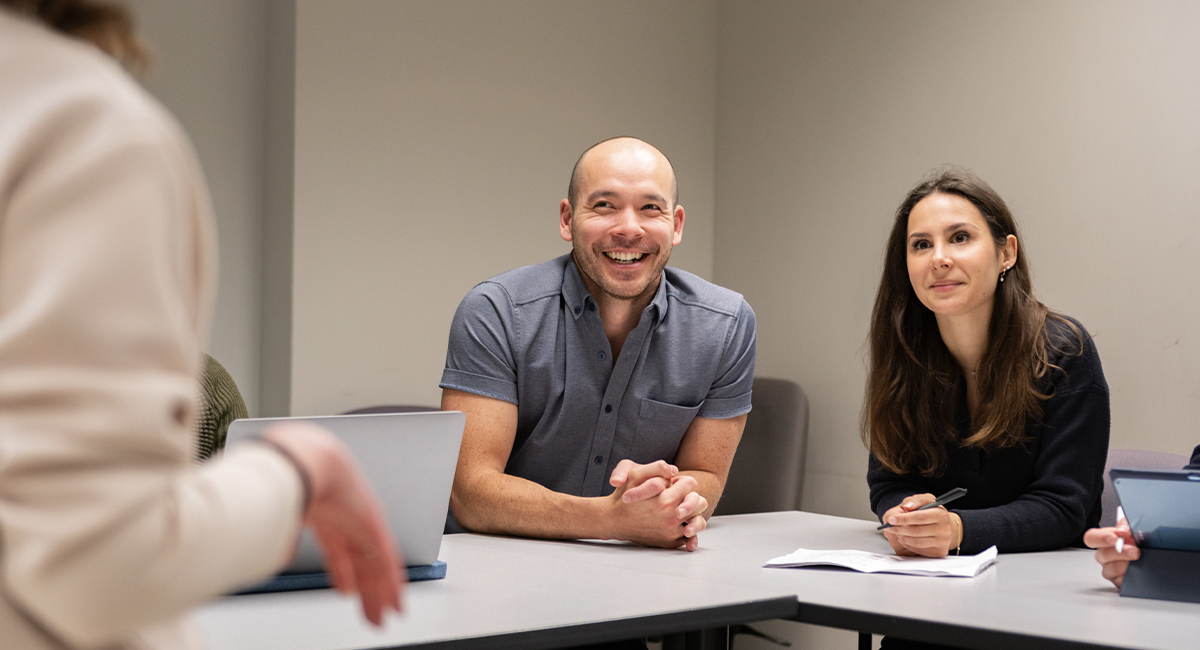 Group of five Schulich Medicine students laughing and talking together indoors, with two standing arm in arm and three seated, enjoying a casual conversation.