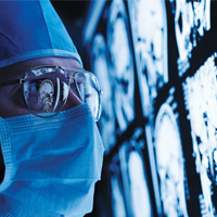 Photograph of a doctor in a surgical mask looking at brain imaging scans 