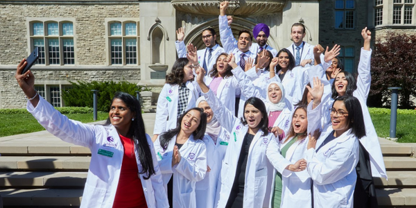 Students preparing a selfie on the steps of a campus building with their new white coats