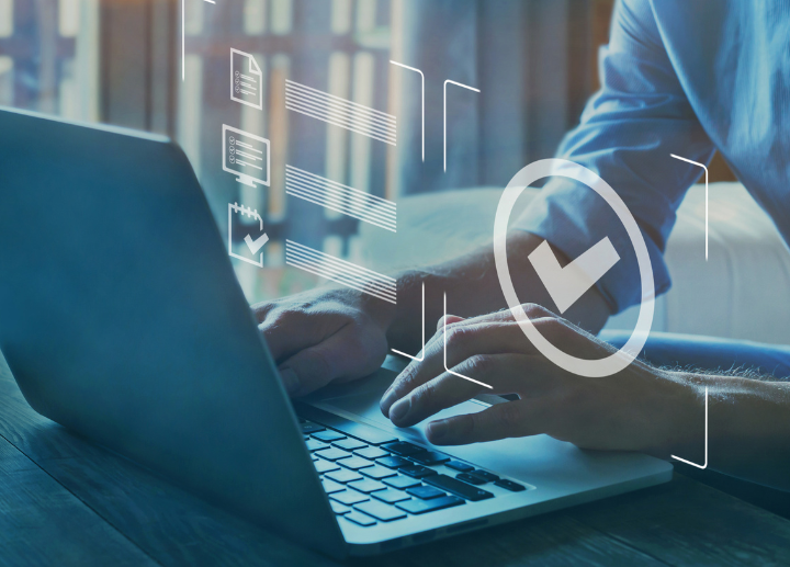 A person sitting at a computer with their laptop facing away from the camera with a superimposed checkmark icon implying achievement