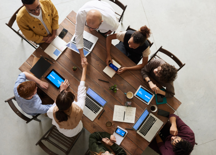 Overhead view of a group of people sitting around a table working together with their laptops and coffee