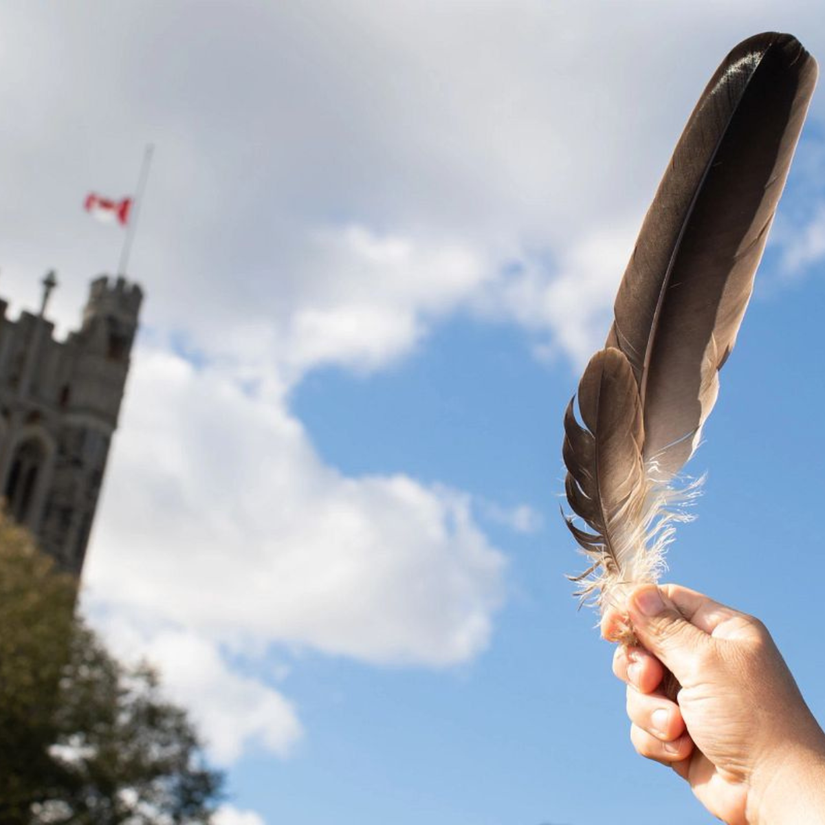 hand holding feather up to the sky