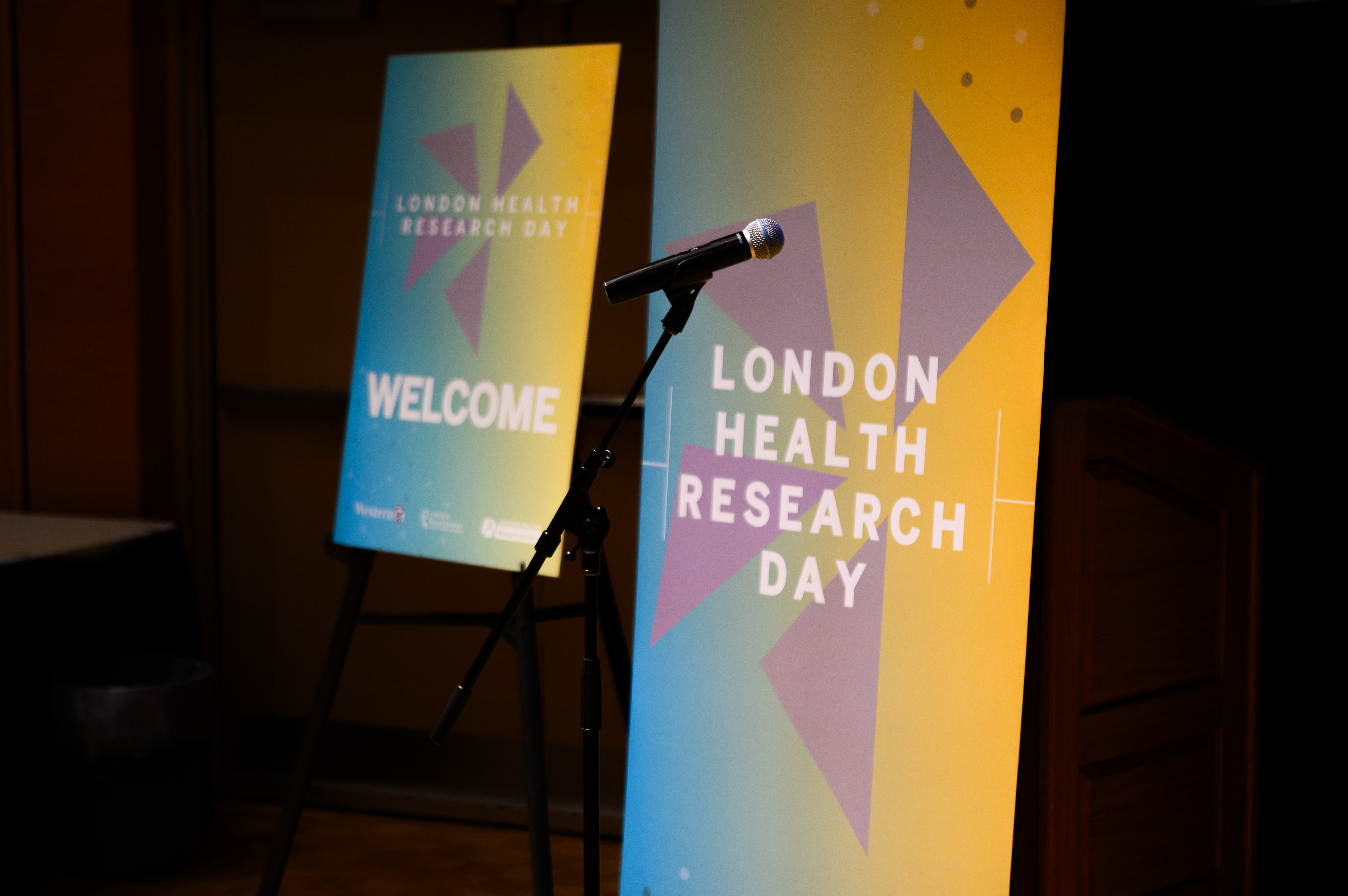 Two colorful “London Health Research Day” welcome banners displayed beside a microphone and podium on a stage.