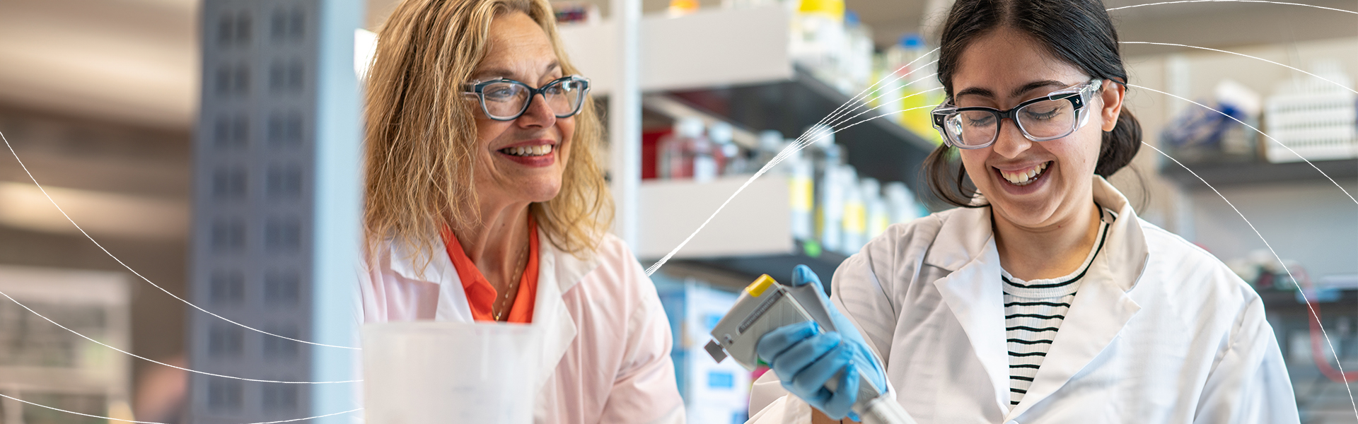 Two researchers working together in a laboratory, smiling as one conducts an experiment with a pipette