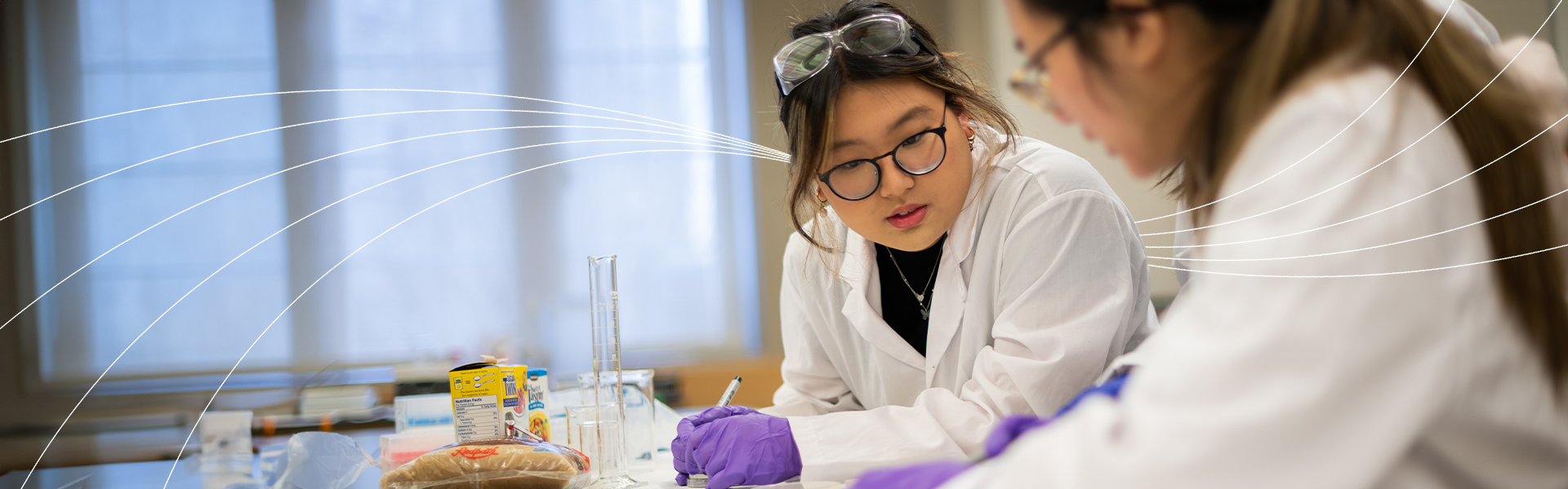 Two students in lab coats and gloves working together on an experiment.