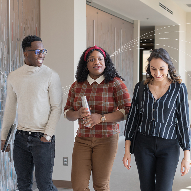 Three students walking and talking in a bright hallway, smiling and holding notebooks and a water bottle, with white curved graphic lines layered over the image background.