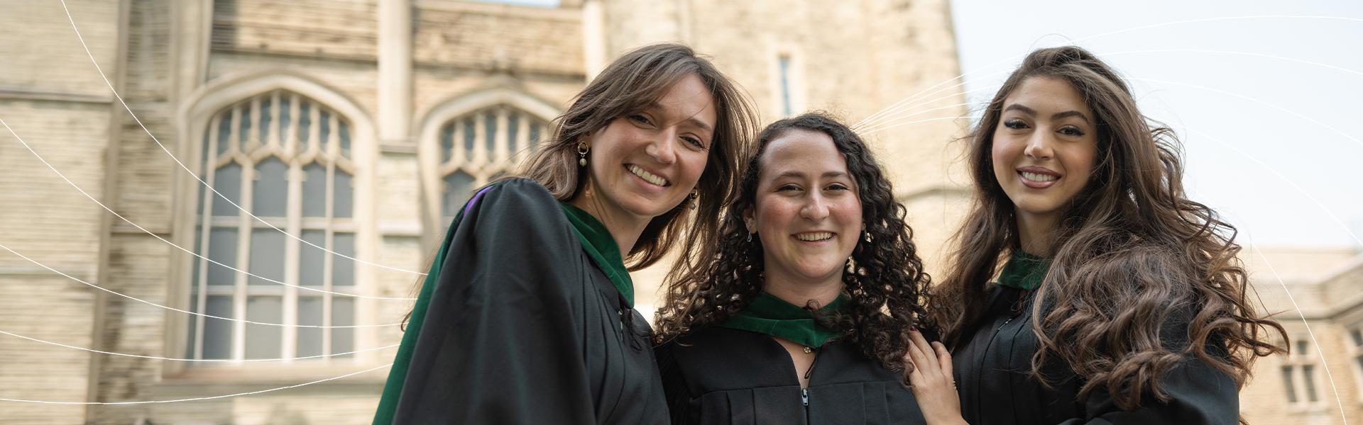 Three graduates celebrate convocation in black gowns and green hoods outside Western University.