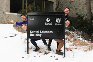 Four students pose by the Dental Sciences Building sign