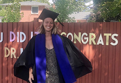 Laura Russell in a cap and gown celebrating her graduation in a backyard