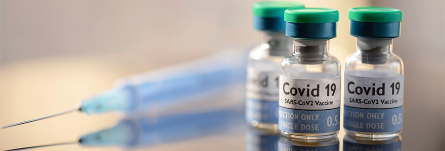 vials of COVID-19 vaccine in the foreground with a synringe in the background