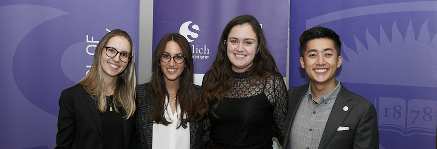 Three female students and one male student posing in front of purple backdrop