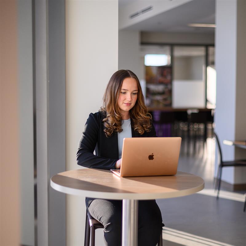 Student working on a laptop at a table in a bright indoor space.
