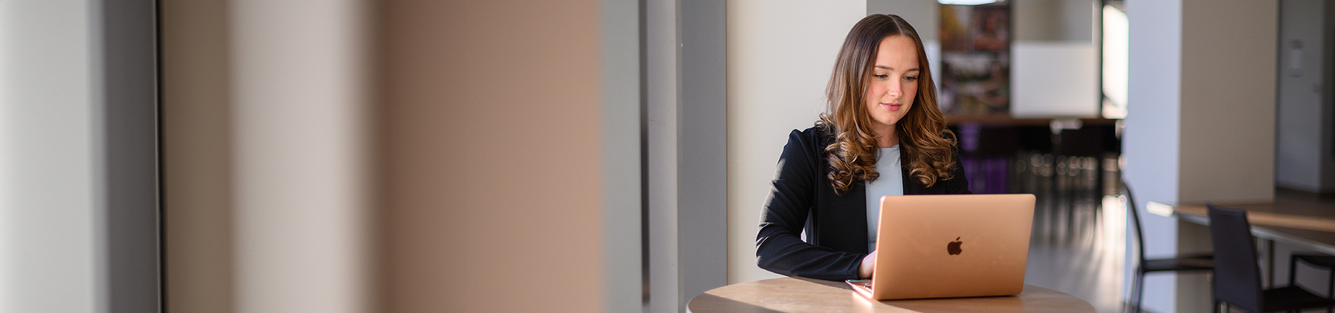 Student working on a laptop at a table in a bright indoor space.