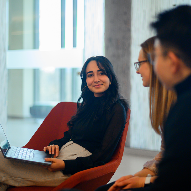 Two students smile and listen attentively as another person speaks in front of them.