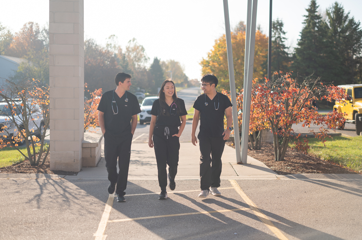 Three medical residents in scrubs walking outside near a clinic building.