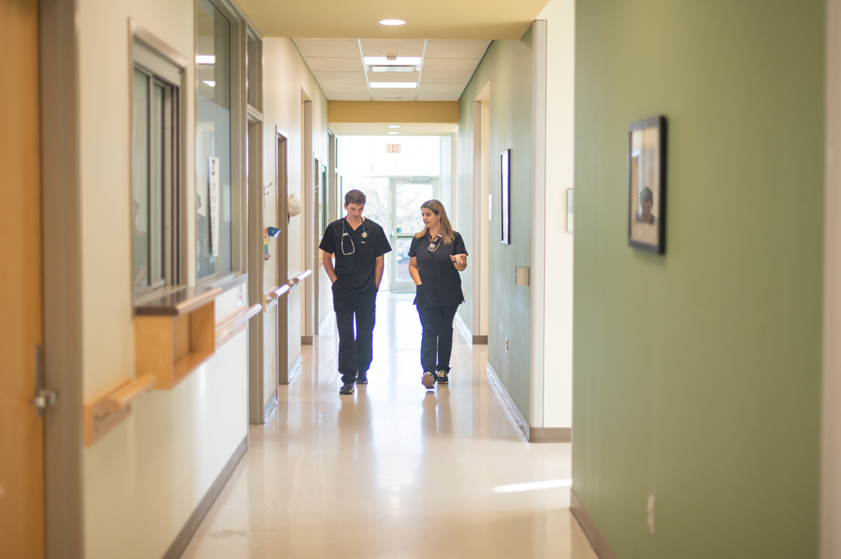 Two healthcare workers walking and talking in a clinic hallway