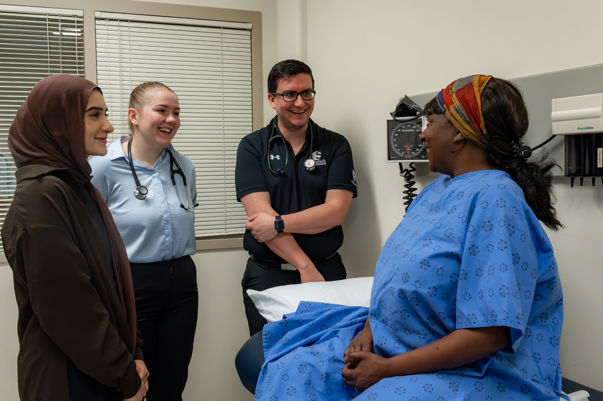 Medical students engage with a patient in a clinical setting, highlighting community-based practice.