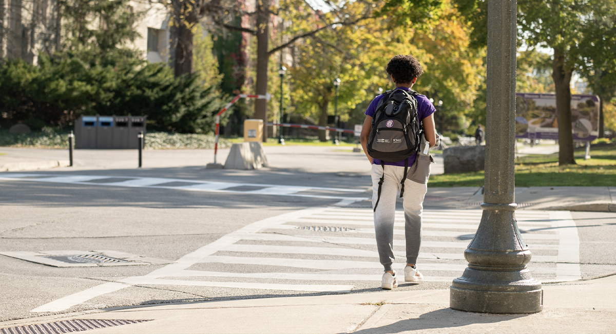 Student walking across a campus crosswalk in autumn