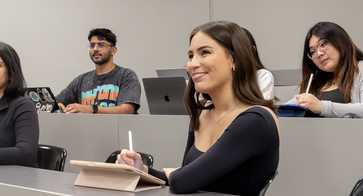 Students attending a lecture, taking notes and using laptops