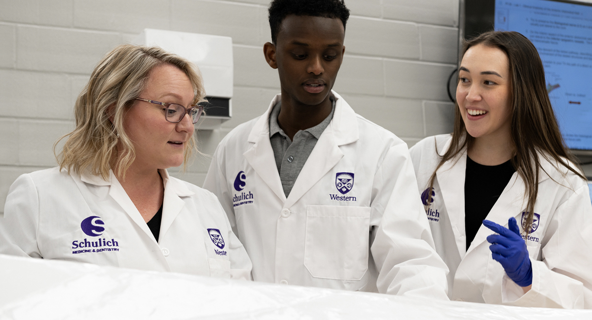 Instructor and students in lab coats reviewing materials in a lab