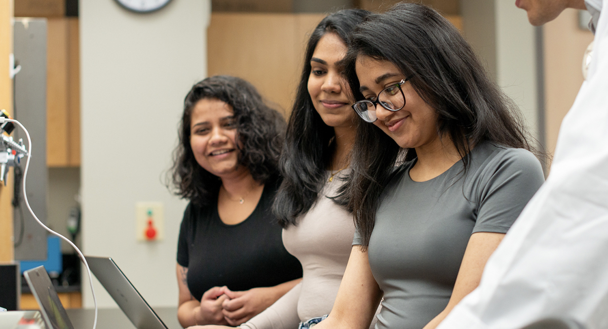 Students reviewing a laptop with an instructor in a lab setting