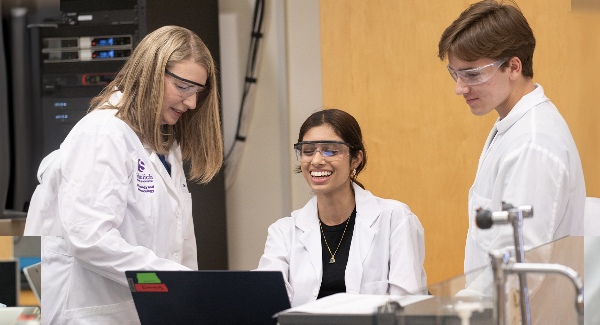 Students in lab coats and safety glasses working together at a bench