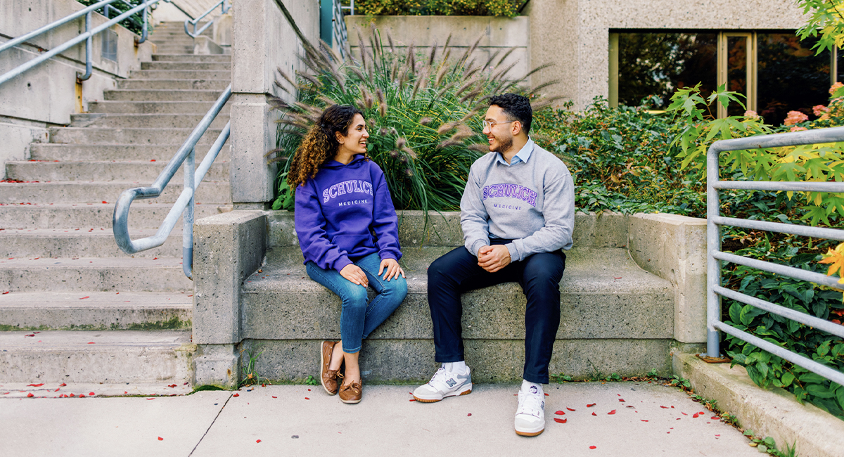Two students sitting and talking outdoors near a building