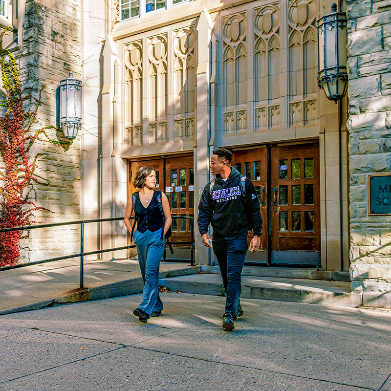 Two students walking and chatting outside the Medical Sciences building, one wearing a Schulich Medicine hoodie