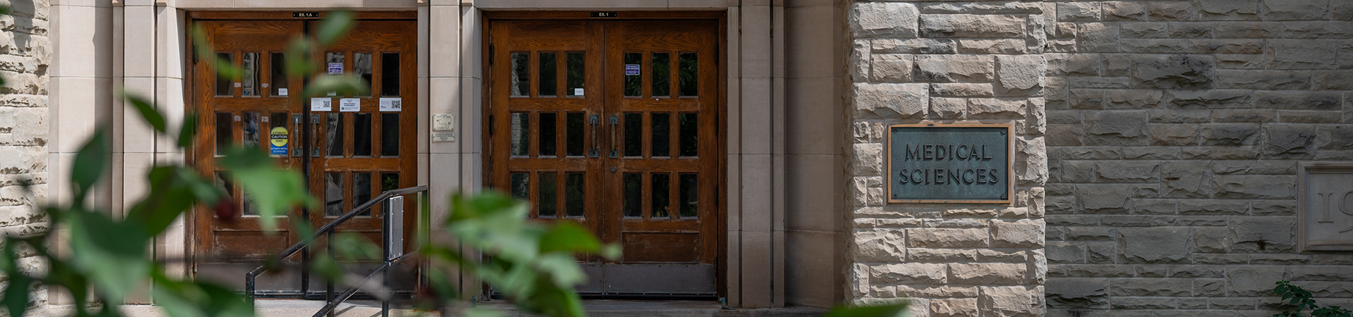 Stone entrance to a Medical Sciences building, with wooden double doors and a metal plaque reading 'MEDICAL SCIENCES