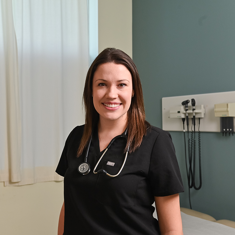 a resident standing in a hospital, smiling, wearing black scrubs and stethoscopes.