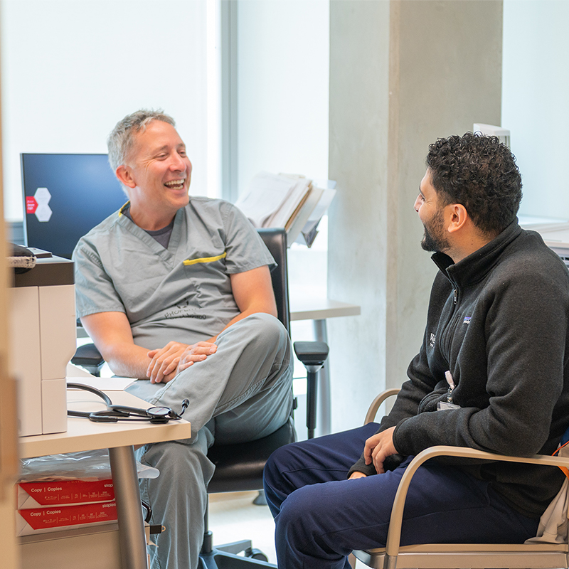 Two healthcare colleagues sitting and laughing together during a relaxed conversation in an office.