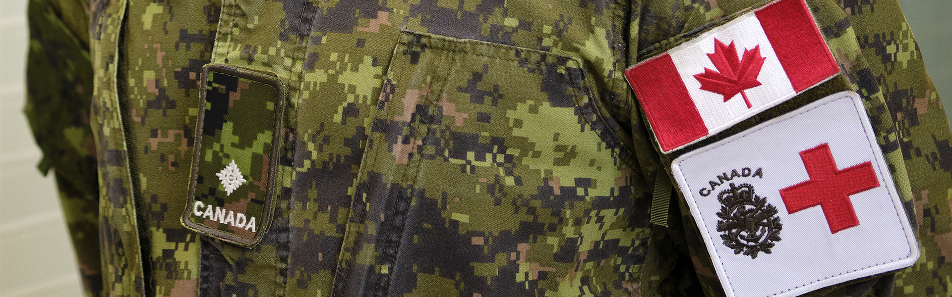Close-up of a Canadian Armed Forces camouflage uniform showing a Canada flag patch and a medical service patch with a red cross.
