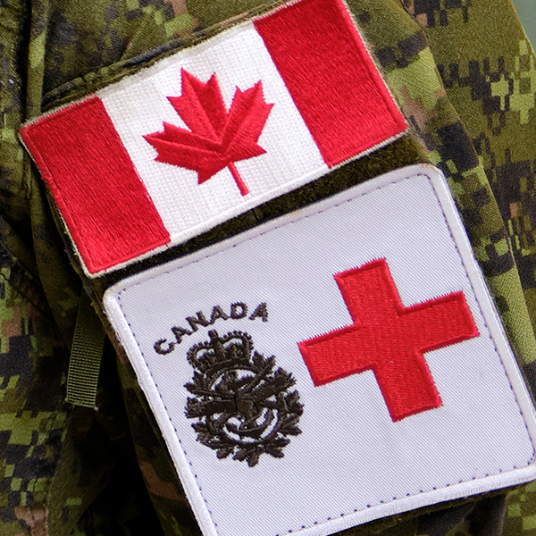 Close-up of a Canadian Armed Forces camouflage uniform showing a Canada flag patch and a medical service patch with a red cross.