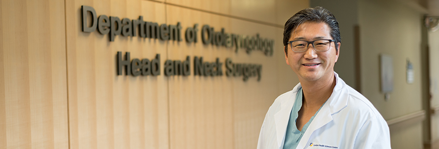 J Yoo standing in the hallway infont of "Department of Otolarynoglogy Head and Neck Surgery" sign.