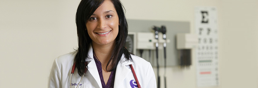 A medical student in a white coat, smiling at the camera