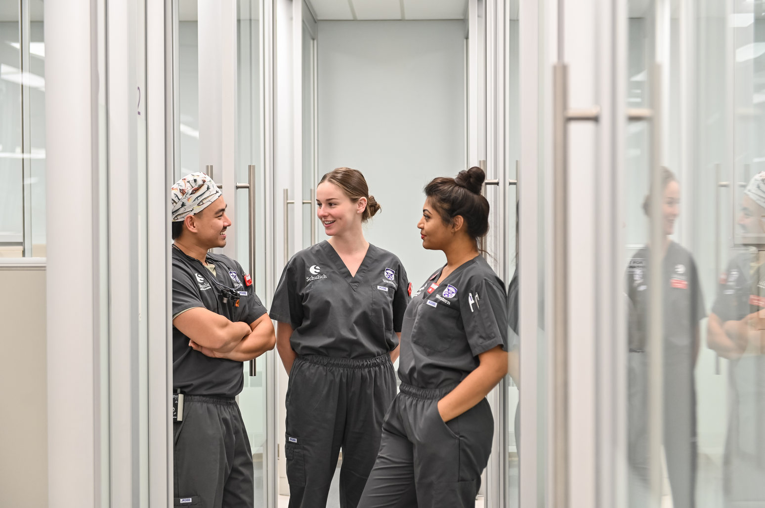 Three Schulich Dentistry students in scrubs talking together in a clinic hallway between treatment bays