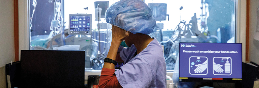 Front line staff looking stressed standing in front of a nursing station with their hands holding their head
