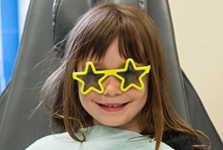 Photo of a child wearing sunglasses sitting on a chair in the clinic